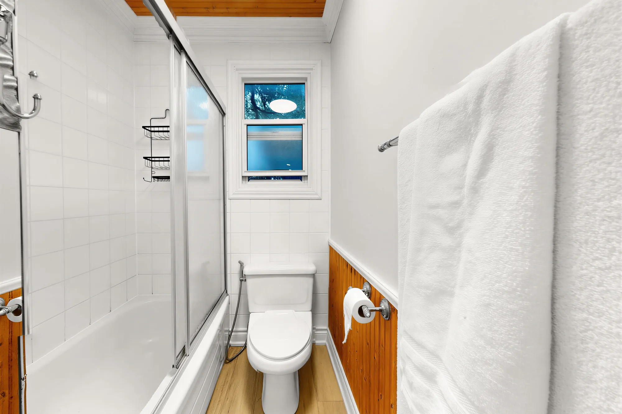 The main bathroom: a tub behind sliding glass doors, white tile, a toilet, a towel