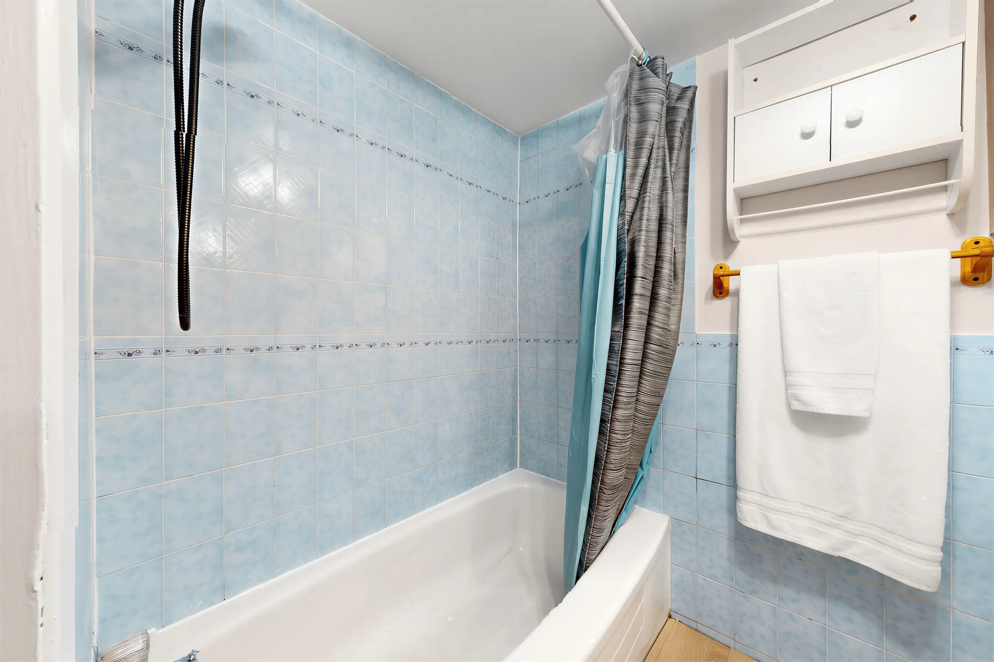 The tub with a shower curtain, blue tile and a white cabinet above the toilet