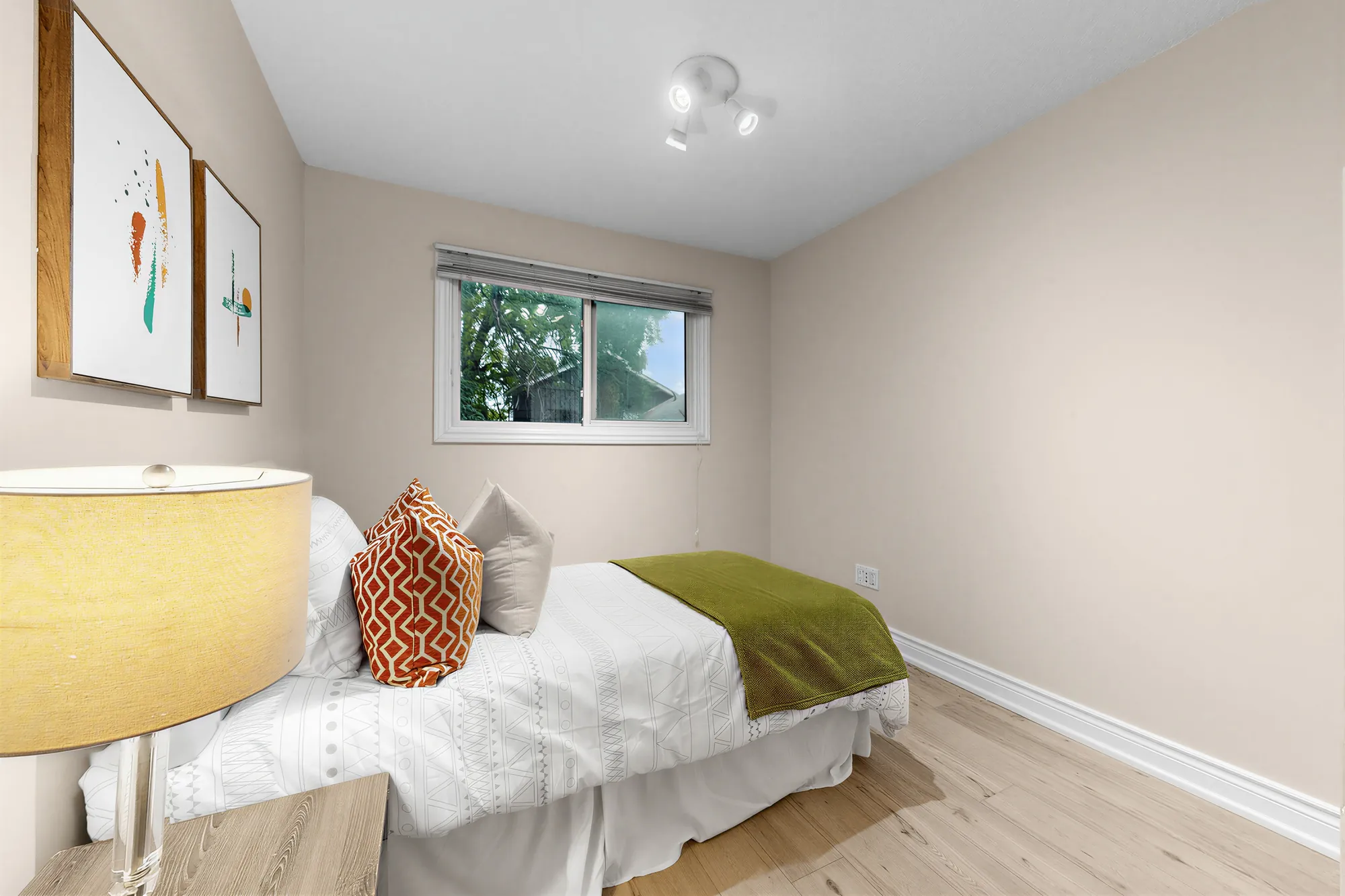 The single bed under the window, a tall lamp in the foreground