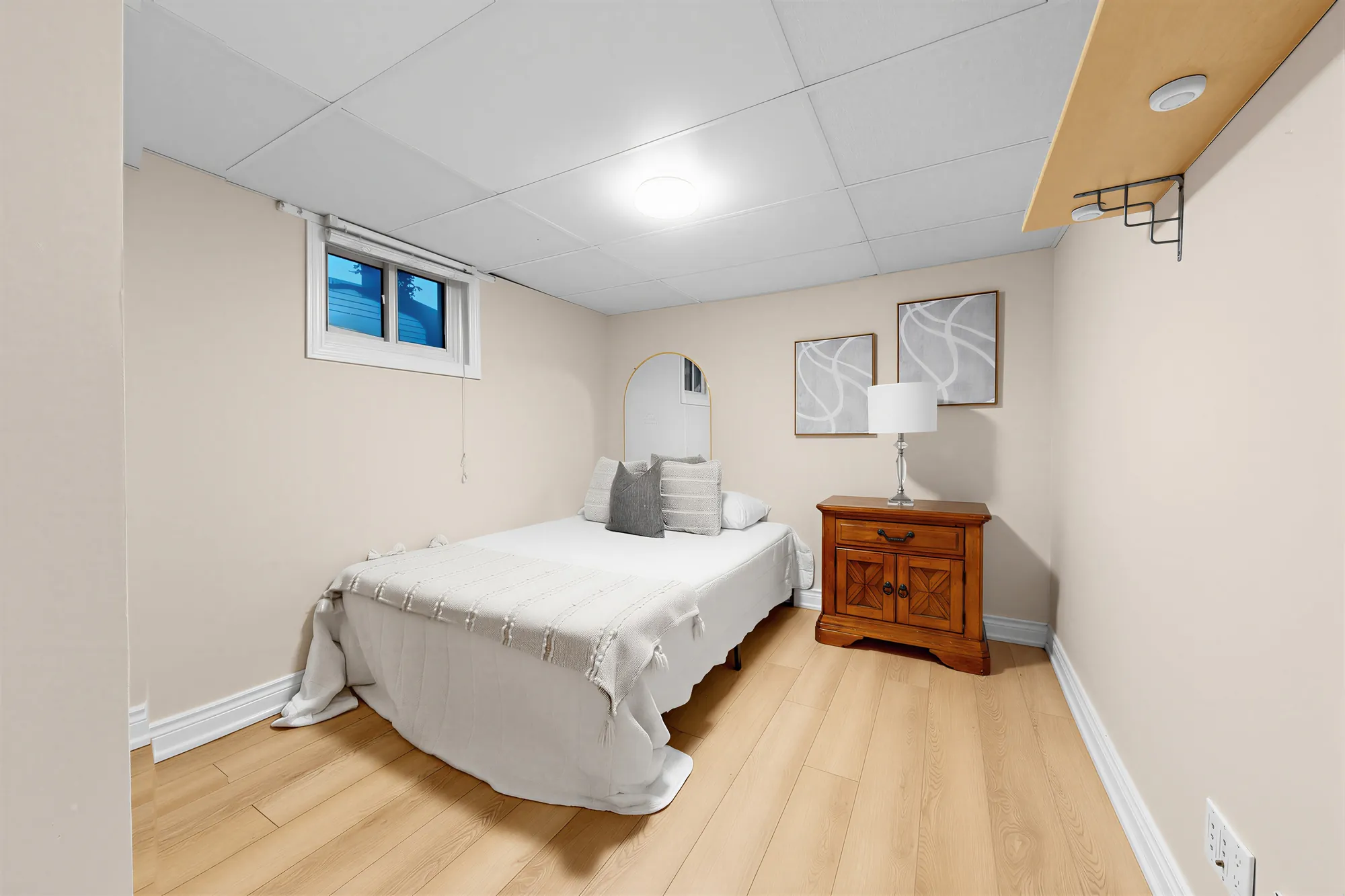 A lower bedroom: a bed and a wooden night table under a small window, framed prints
