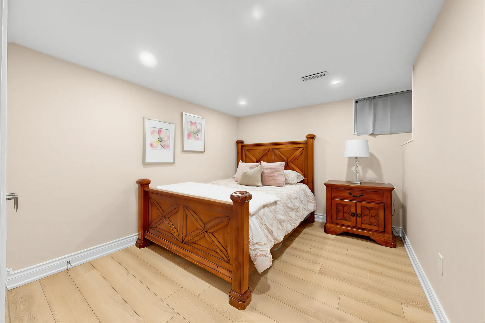 The second lower bedroom: a carved wooden bed and night table, two framed prints, a small window