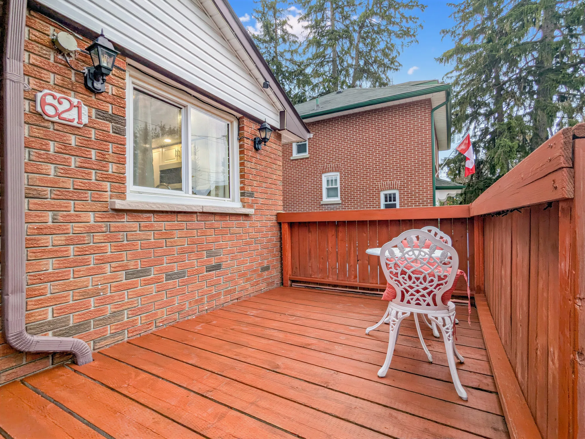 The front deck: stained boards and railings, a white wrought-iron chair, the brick wall with the number 621 and a window