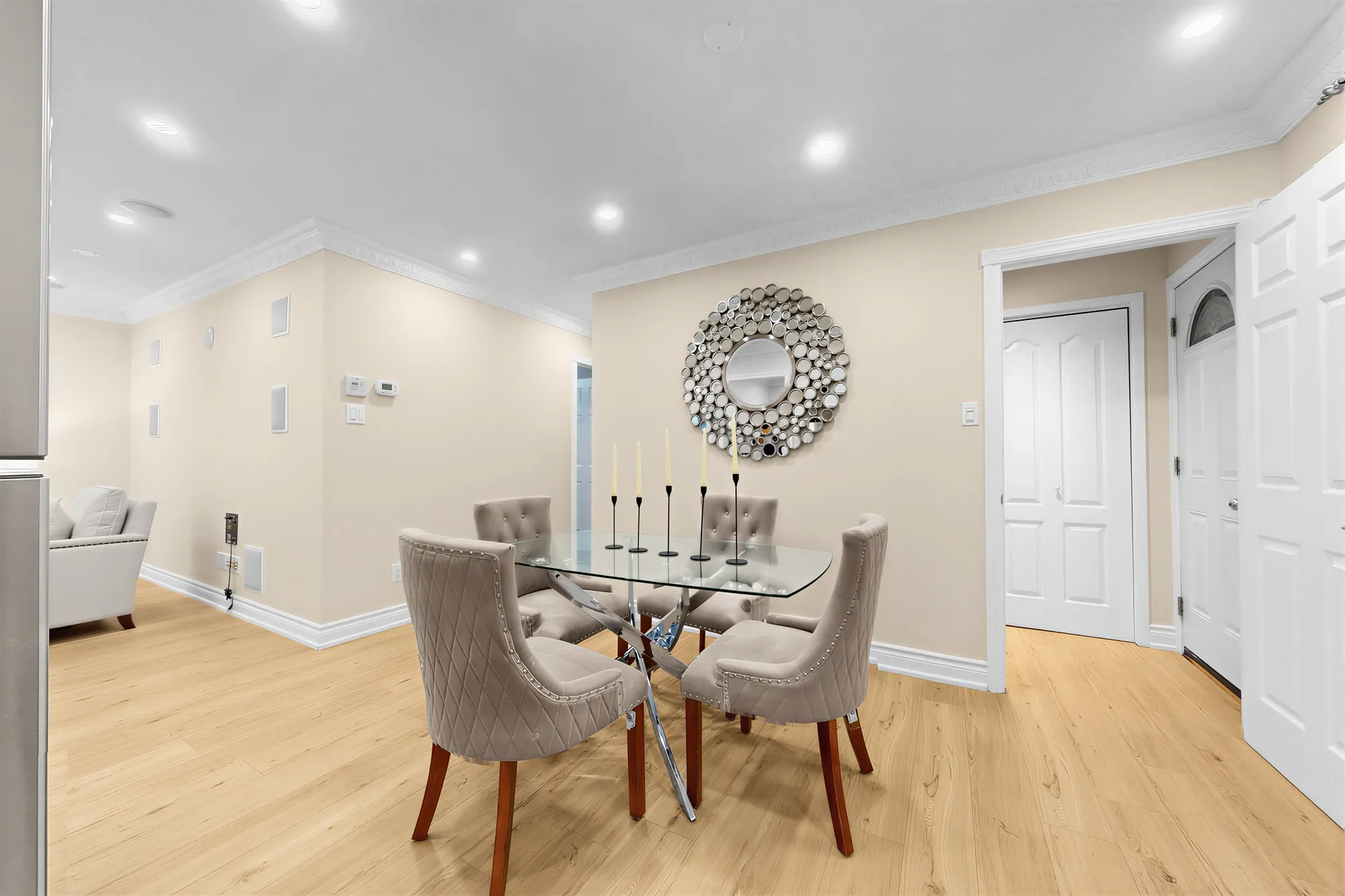The dining room: a glass table with four upholstered chairs, a round mirror, the living room at the left, doors at the right