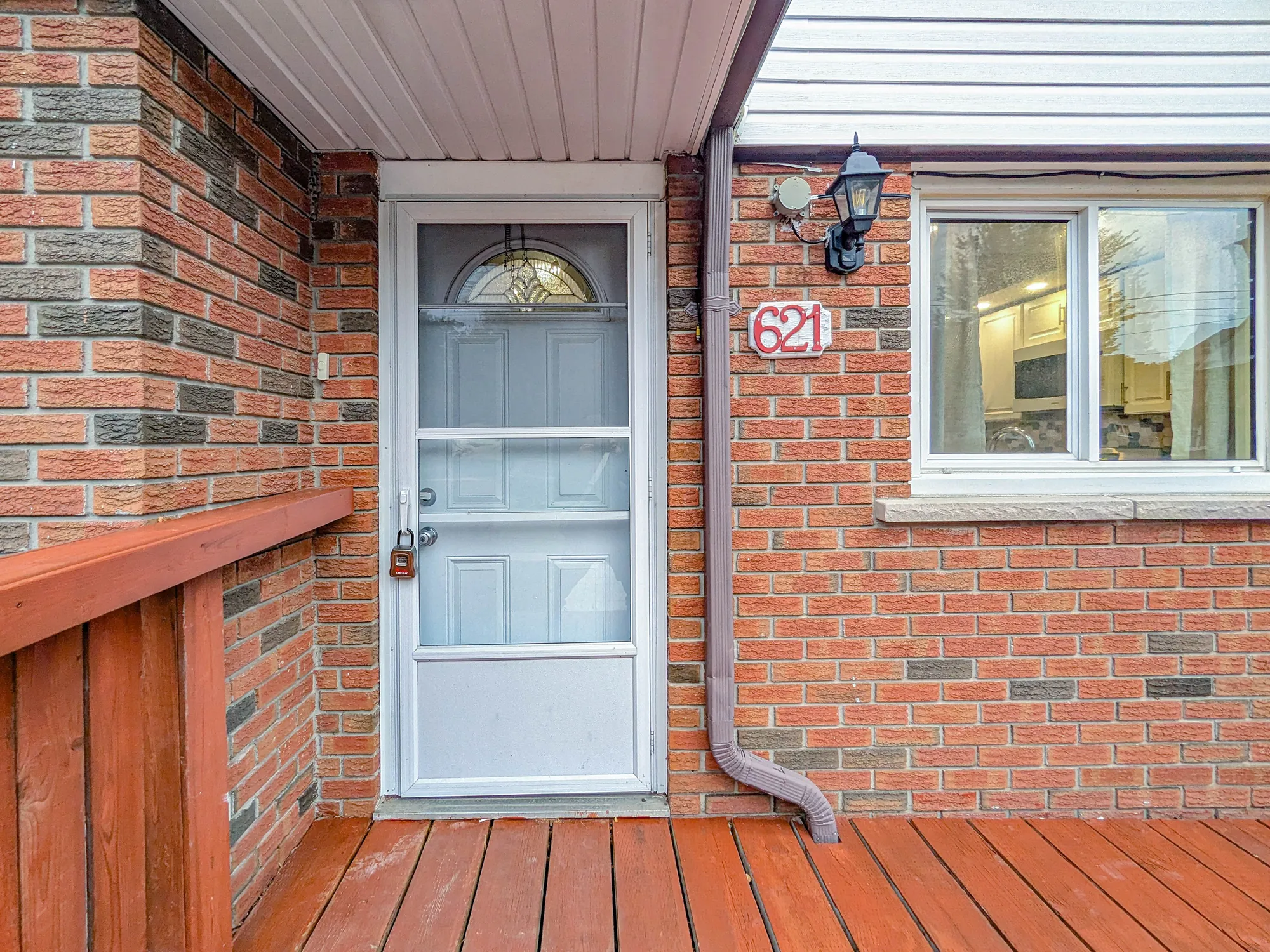 The front door: a white storm door over a door with a half-moon window, the number 621 on the brick, a wall lantern, the deck railing