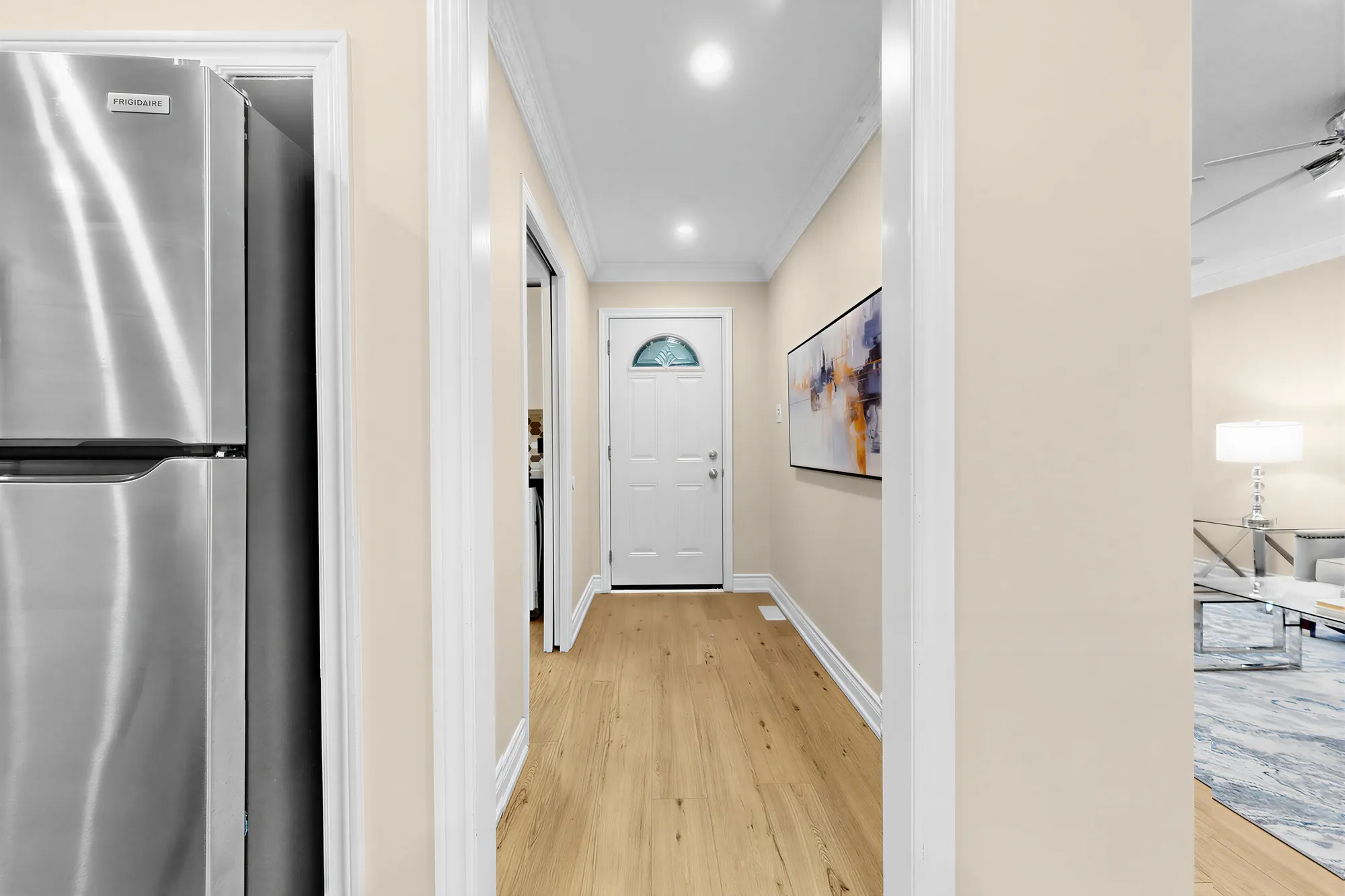 Down the foyer to the front door, a stainless fridge at the left, the living room through the opening at the right