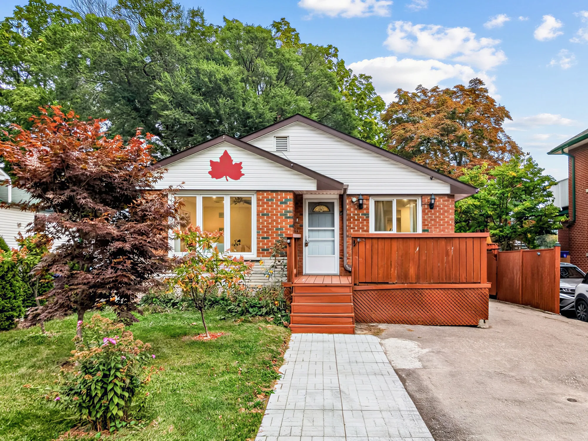The front of 621 Byron Street South: a brick bungalow with white siding and a red maple leaf in the gable, a wide window at the left, a white front door, a stained wood deck across the front, a Japanese maple on the lawn; a silent excerpt of the walkthrough video plays over it