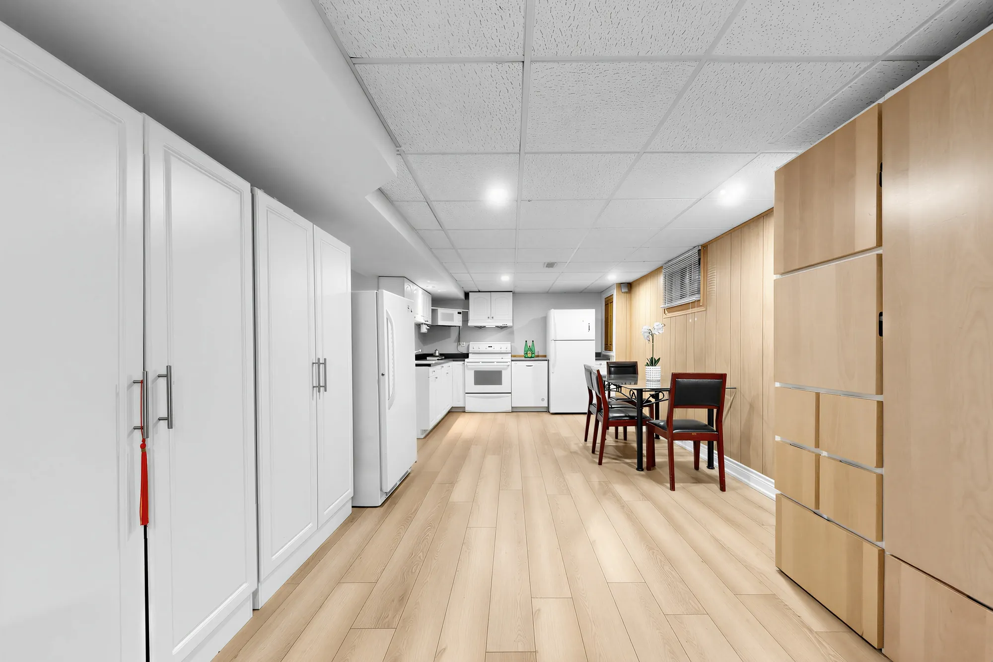 Tall white storage cabinets along the left wall, the kitchen and the dining table at the far end, wood panelling at the right
