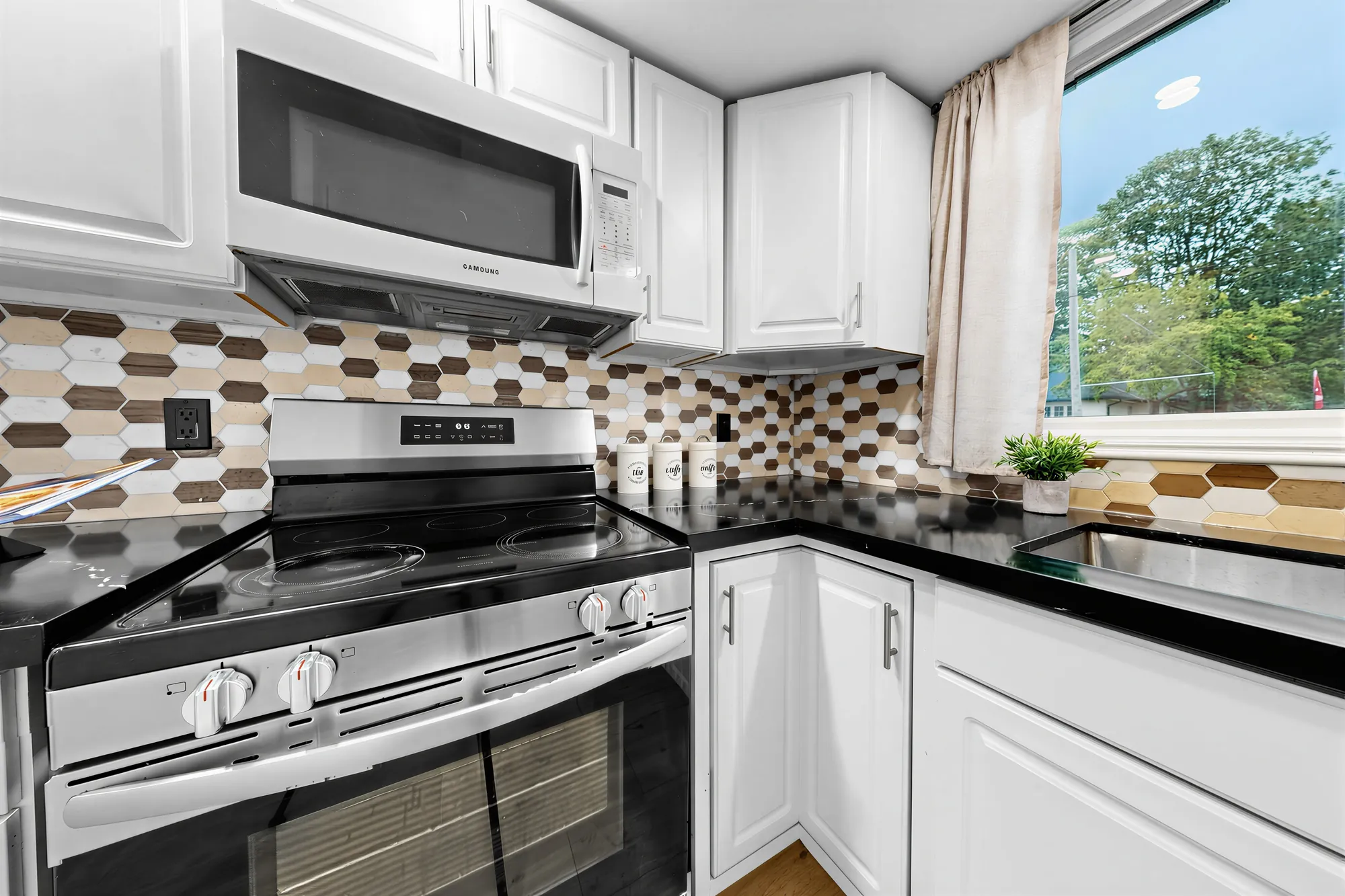 The kitchen: white shaker cabinets, black counters, a backsplash of hexagon tiles, a stainless range under a microwave, a window over the sink