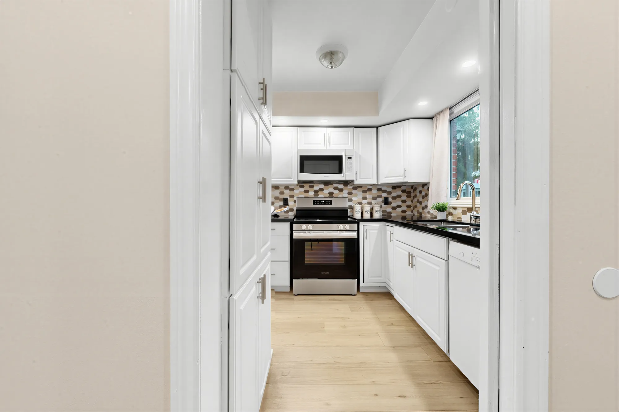 The kitchen through its doorway: the range, the microwave and the white cabinets, a window at the end