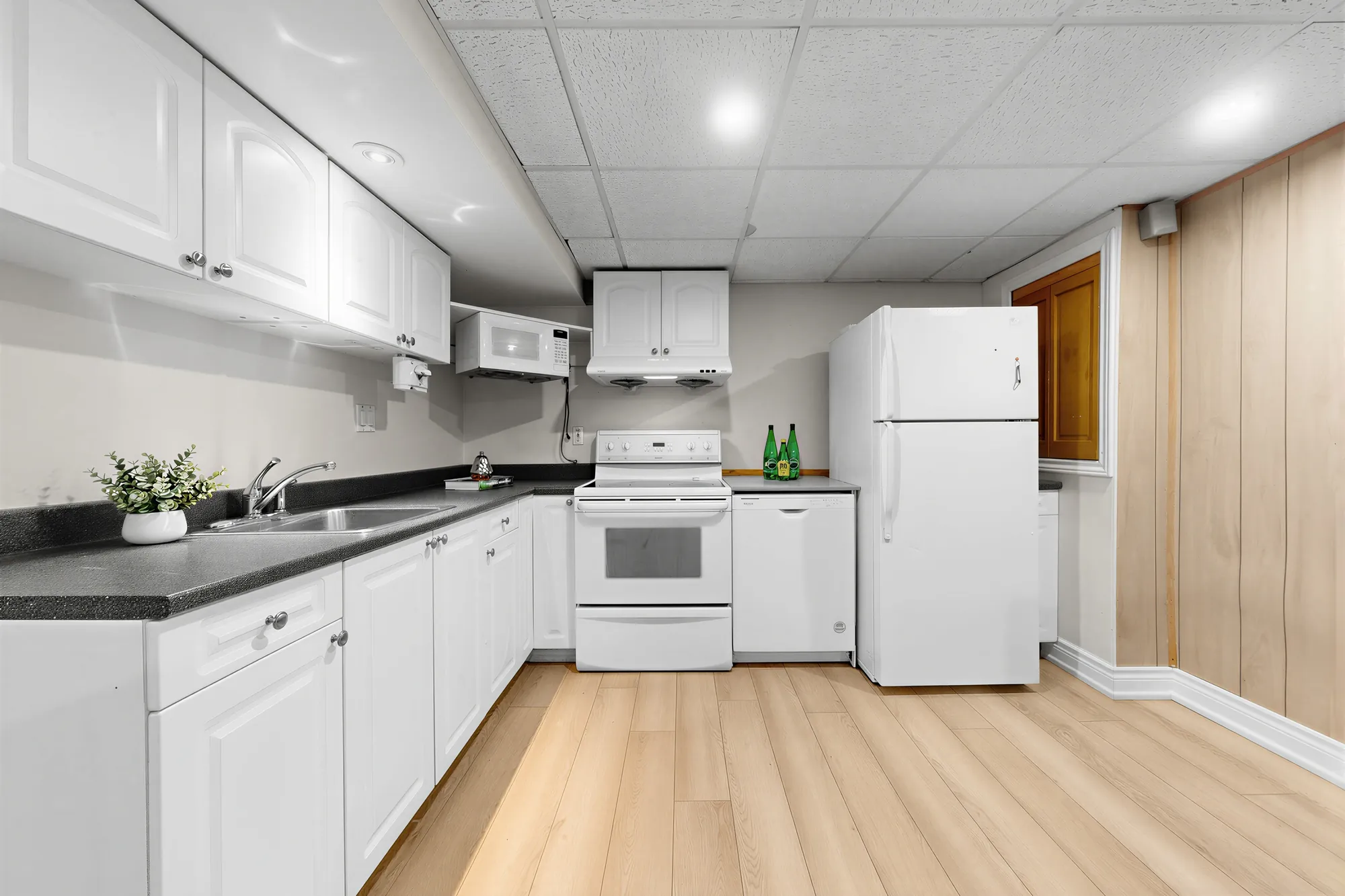 The lower kitchen: white cabinets, black counters, a white range, fridge and dishwasher, a microwave over the range
