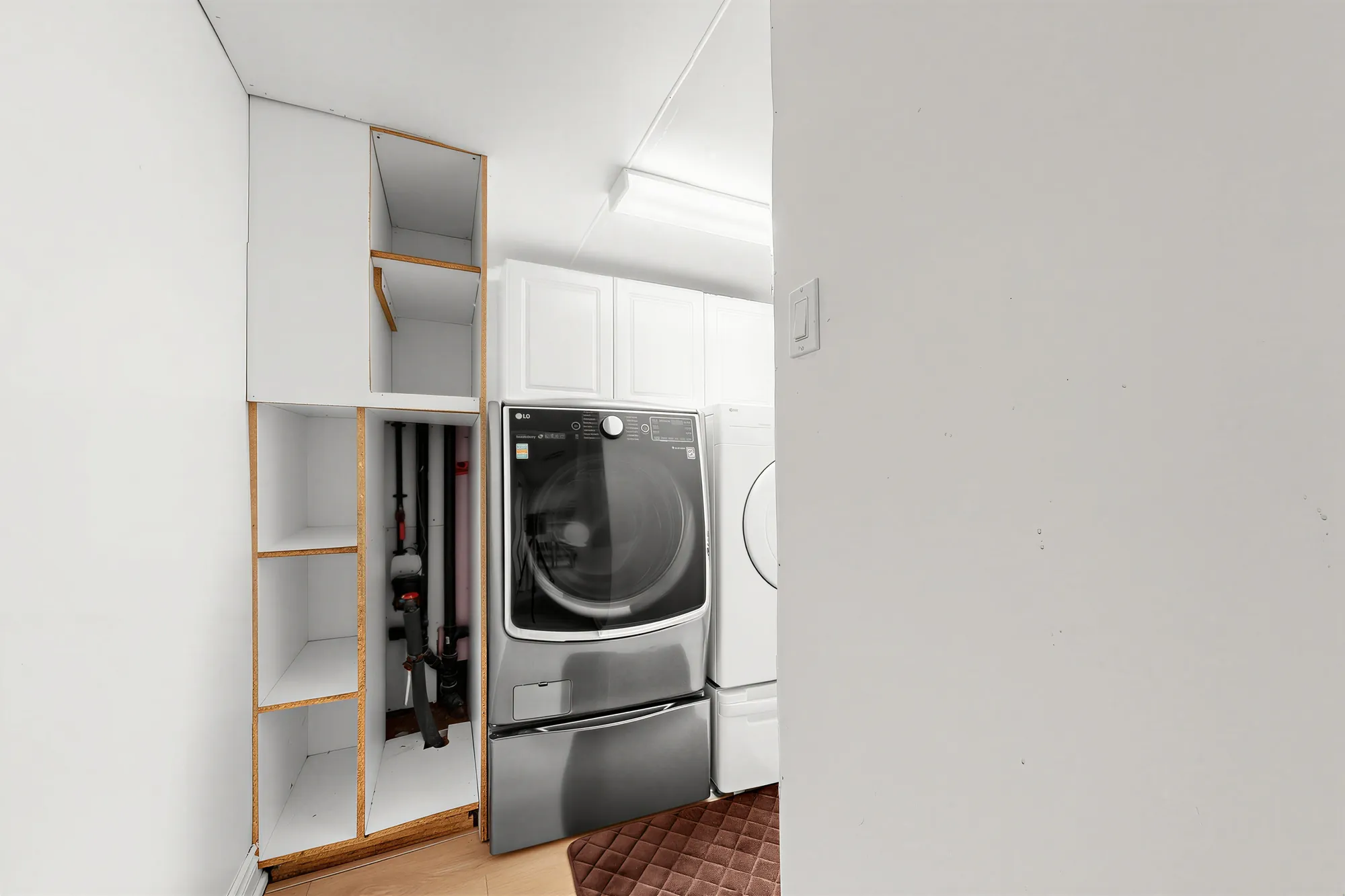 The laundry: a front-load washer on a pedestal beside a dryer, white cabinets above and open shelves at the side